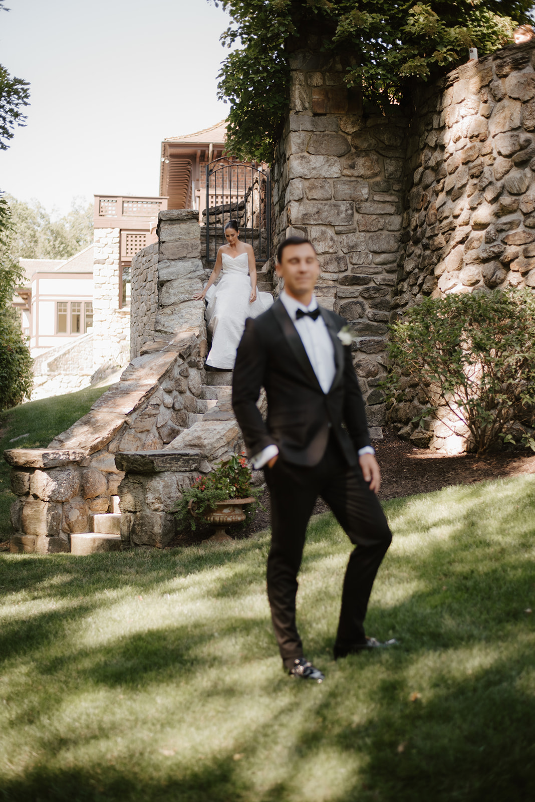Bride walking down historic stone stairs for a first look while the groom stands waiting in the foreground.